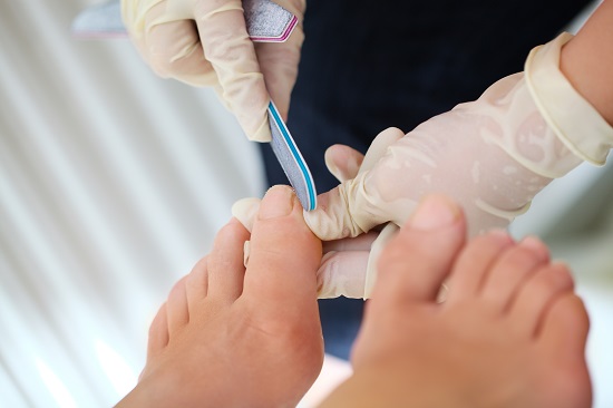 Macro shot of female feet during professional pedicure. Filing procedure at beauty spa salon